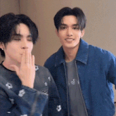 two young men are standing next to each other in a room . one of the men is covering his mouth with his hand .