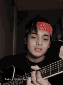 a young man with a bandana on his head is playing a guitar