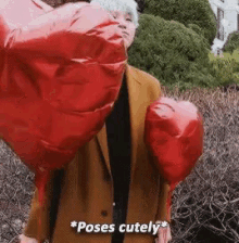 a man is holding two red heart shaped balloons and says poses cutely .