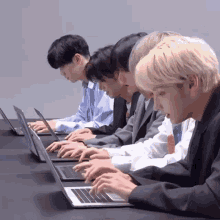a group of men are sitting at a table typing on laptops .
