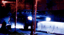 a car is driving down a street at night with a cw logo in the corner