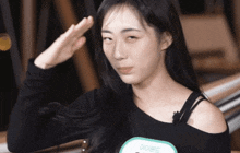 a woman wearing a black off the shoulder top salutes with her hand on her forehead