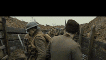 a group of soldiers are standing in a trench talking to each other while wearing helmets .