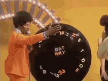 a man in an orange suit is holding a microphone in front of a large black wheel that says dat way .