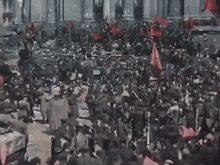 a large crowd of people are gathered in front of a building with red flags