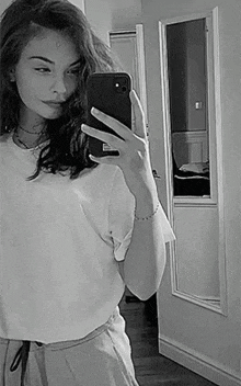 a woman is taking a selfie in front of a mirror with her cell phone .