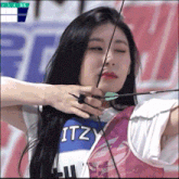 a woman holding a bow and arrow wearing a itzy shirt