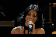 a woman sings into a microphone on a stage with drums in the background
