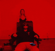 a woman stands behind a man with his arms outstretched and a t on his shirt