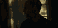a man in a black shirt is standing in a dark room with a light behind him .