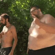 a shirtless man is standing next to a very fat man who is smoking a cigarette .