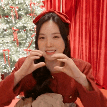 a woman wearing a red headband is making a heart shape with her hands in front of a christmas tree