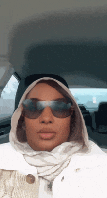 a woman wearing sunglasses and a white scarf is sitting in the back seat of a car