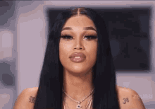 a woman with long black hair and a tattoo on her arm is wearing a necklace and looking at the camera .
