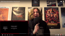 a young man speaking into a microphone in front of a wall with posters for avengers and inception