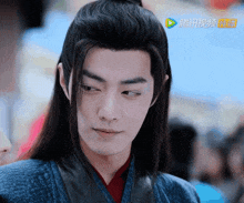 a man with long hair and a ponytail is wearing a blue jacket and red shirt .