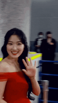 a woman in a red off the shoulder dress is waving her hand .