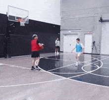 two men are playing basketball in a gym and one is wearing a red jersey