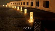 a row of lit candles are lined up on the side of a road in a dark area