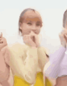 a woman in a yellow skirt is covering her mouth with her hands while standing next to a man in a purple shirt .