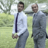 two men in suits are standing next to each other on a grassy field .