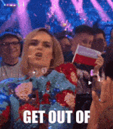 a woman is holding a flag in front of a crowd and the words get out of are visible