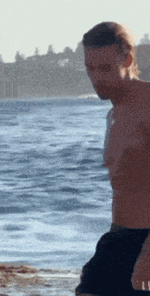 a shirtless man is walking on the beach near the water