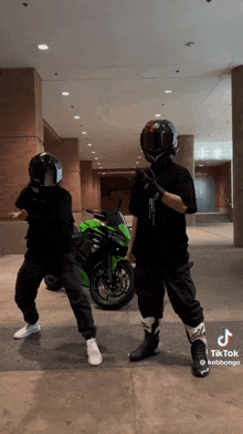 two men wearing helmets are standing next to a green motorcycle ..