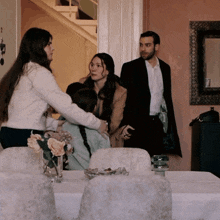 a group of people are standing around a table with a vase of flowers on it