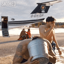 a shirtless man carrying a bucket of water in front of a plane that says d-gh/dp