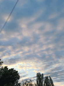 a cloudy sky with trees in the foreground and power lines in the background