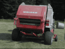 a red welger hay baler is sitting in a grassy field