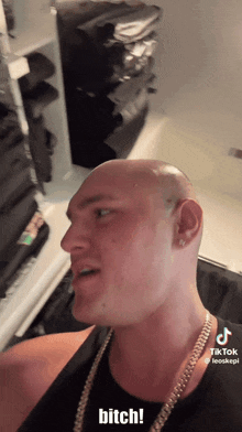 a man with a shaved head and a gold chain says bitch
