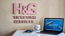 a sign that says h & g ticketing services is above a laptop