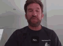 a man with a beard is wearing a black t-shirt that says `` no '' on it .