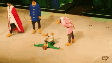 a man in a red cape is standing next to a man in a pink shirt who is laying on the ground .
