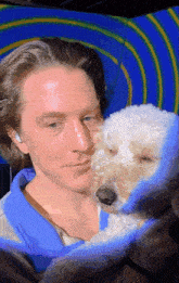 a man in a blue shirt holds a small white dog in his arms