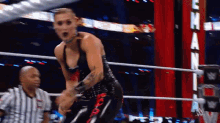 a wrestler is standing in a ring with a referee behind him and a sign that says eh on it