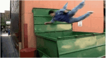 a man is jumping into a green dumpster with a sign that says no dogs