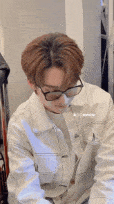 a man wearing glasses and a white jacket is sitting in a room .