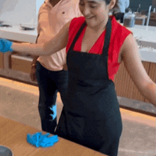 a woman wearing an apron and blue gloves stands in front of a wooden table