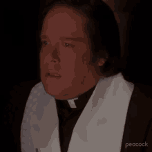 a man in a priest 's robe is making a funny face with his eyes closed in a dark room .
