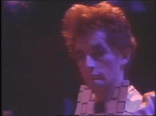 a close up of a man 's face in a dark room with purple lights behind him .