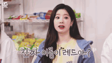 a girl in a yellow shirt and a blue jacket is making a funny face in front of a shelf full of snacks