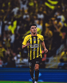a soccer player wearing a yellow and black striped jersey that says roshn sur