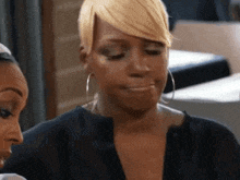 a woman with blonde hair and hoop earrings is making a funny face while sitting next to another woman .