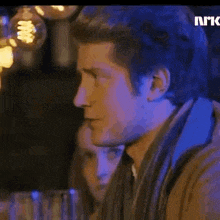 a man is sitting at a table in a dark room with a woman behind him .