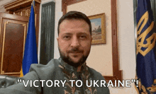 a man with a beard says " victory to ukraine " in front of a flag