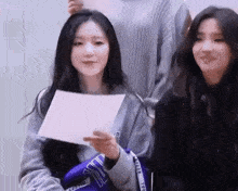 two girls are sitting next to each other holding a piece of paper .
