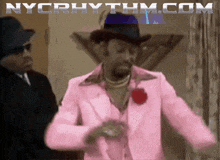 a man in a pink suit is dancing with nycrhythm.com in the background